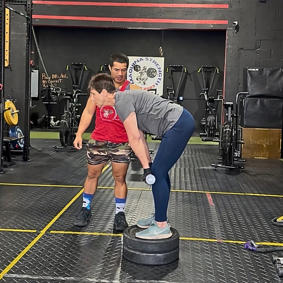 Coach Carlos coaching a hip hinge with a dumbbell at Máquina Strength