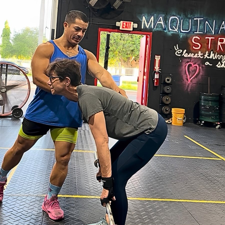 Coach Carlos teaching a member in her sixties to hold position and brace over a barbell at Máquina Strength