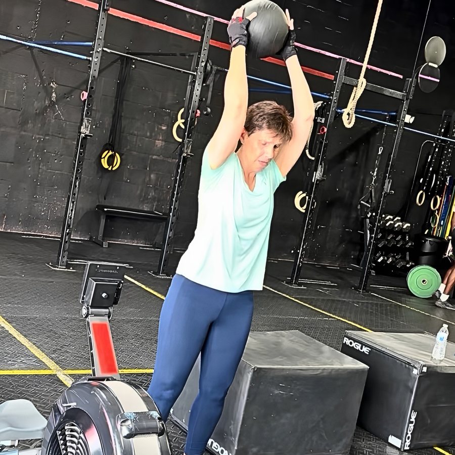 A member in her sixties pressing a medicine ball overhead during a conditioning set at Máquina Strength